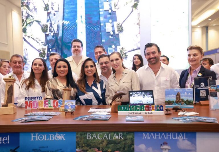 A group of diverse individuals representing various Caribbean destinations pose together at a travel expo with promotional materials in front of them.