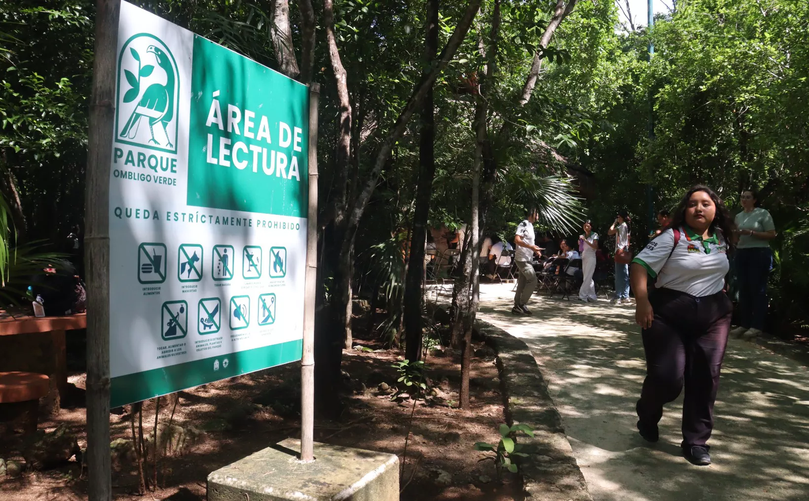 A sign indicating the 'Reading Area' in a park surrounded by greenery, with people in the background.$# CAPTION