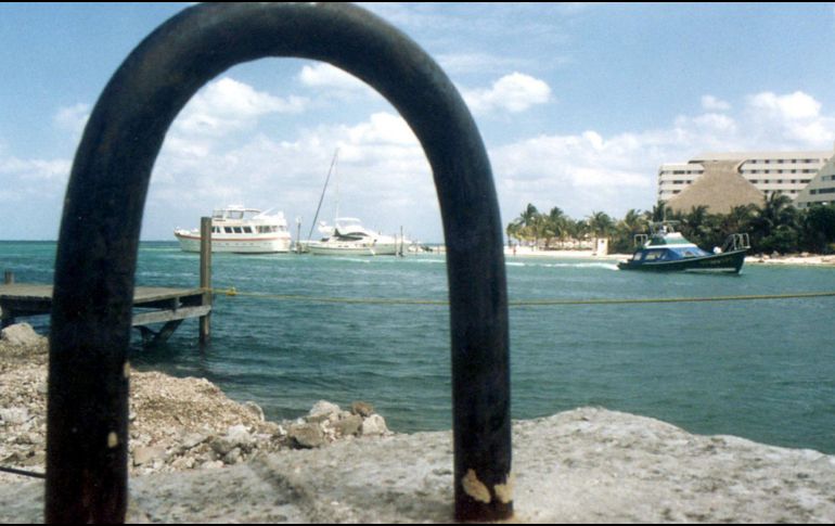 A view through an arch of a boat in the water and a building along the shore in a tropical setting.$# CAPTION