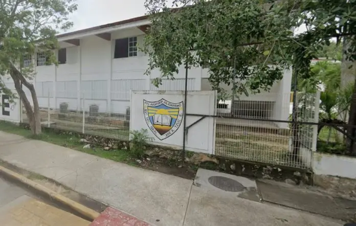 Exterior view of a school building featuring a logo on a fence, surrounded by greenery