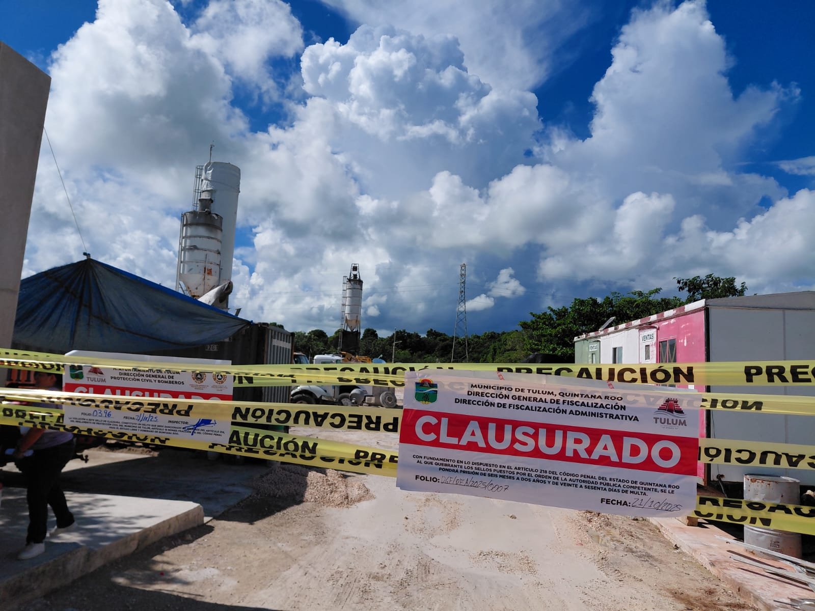 A closure notice is displayed on a construction site in Tulum, surrounded by caution tape and equipment under a cloudy sky.$#$ CAPTION