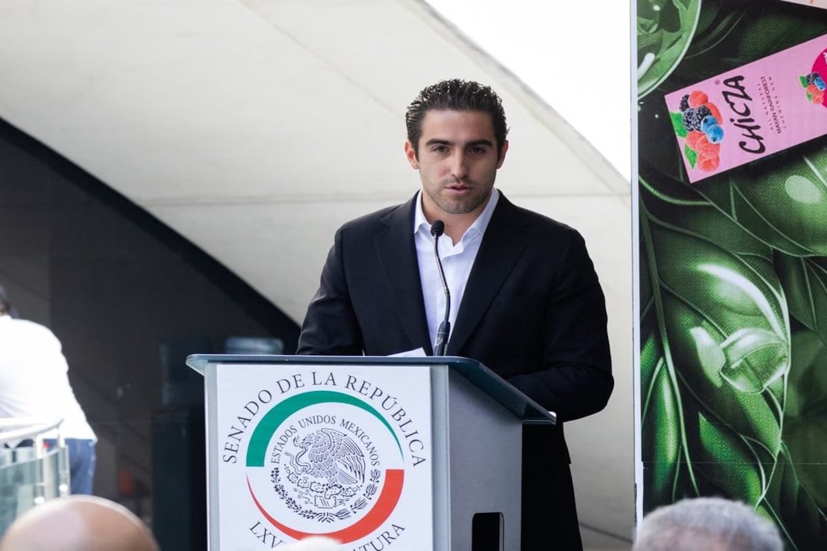 a man in a black suit speaking at a podium with the emblem of the Senate of Mexico in the background