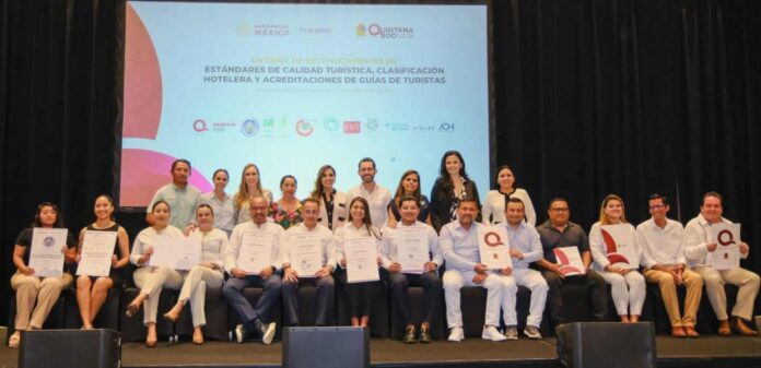 Group of individuals posing on stage, holding certificates at a tourism quality standards event in Mexico.$#$ CAPTION