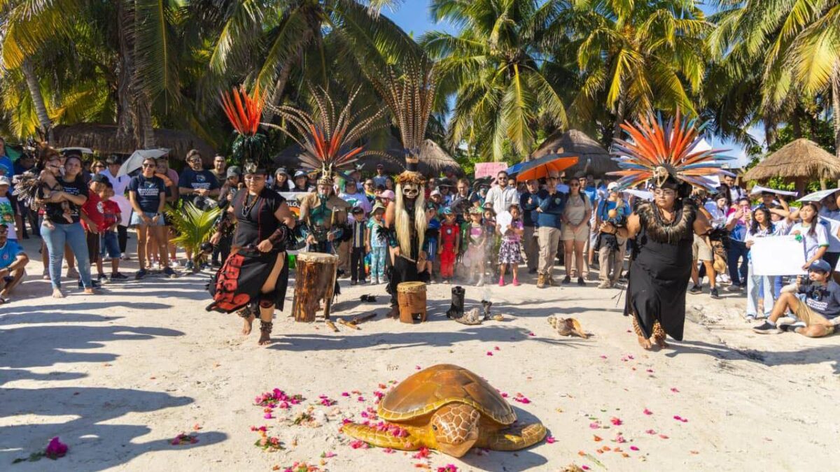 a beach scene with performers in traditional attire celebrating with a painted turtle and an audience-27102025