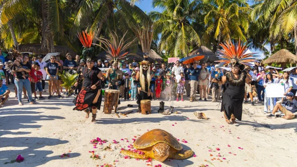 a beach scene with performers in traditional attire celebrating with a painted turtle and an audience-27102025