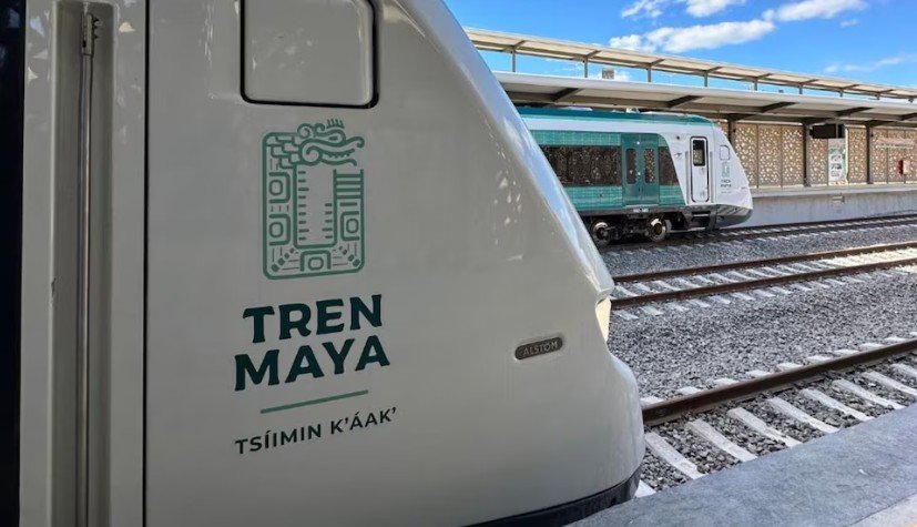 Close-up of a Tren Maya train with its logo visible at a train station, showcasing the sleek design and surroundings in the background.