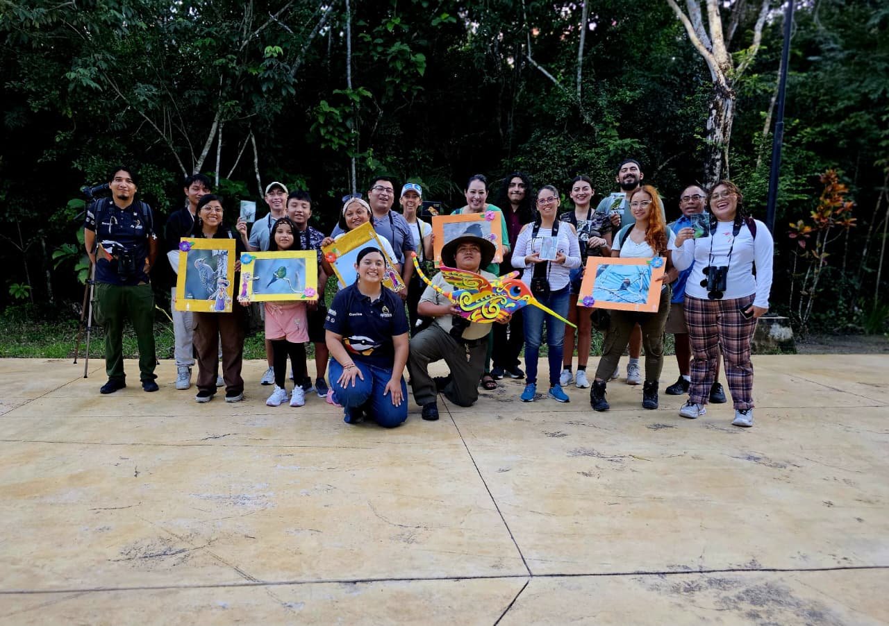 A group of people holding colorful artwork depicting birds in a lush green environment-
