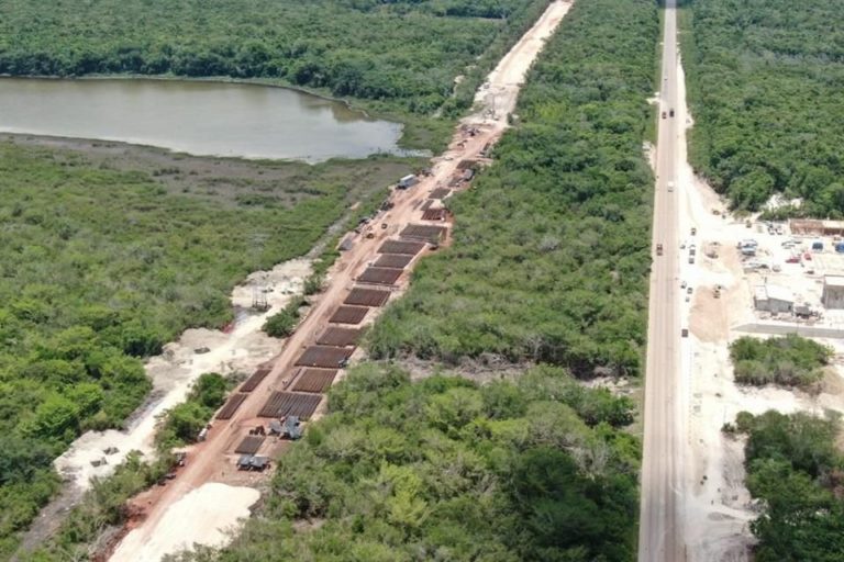 Aerial image showing construction activity alongside a roadway in a lush green area, with a river visible nearby.$