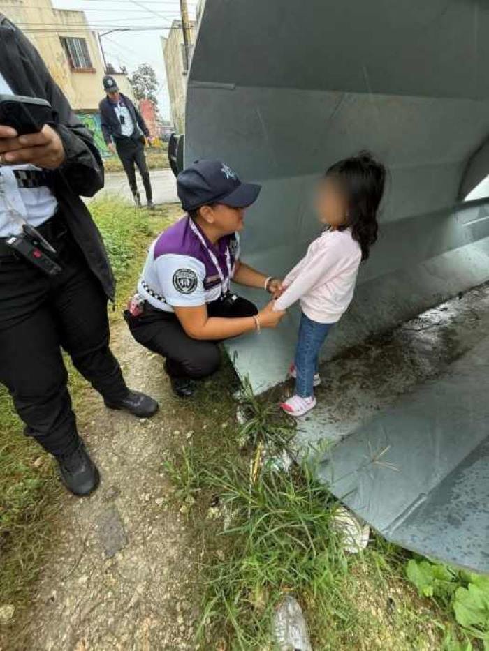 A police officer kneels beside a young girl in a gray shelter, offering comfort and support while others observe nearby.$# CAPTION