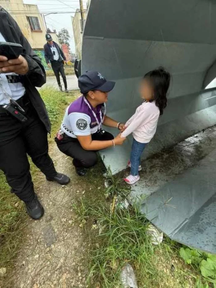 A police officer kneels beside a young girl in a gray shelter, offering comfort and support while others observe nearby.$# CAPTION