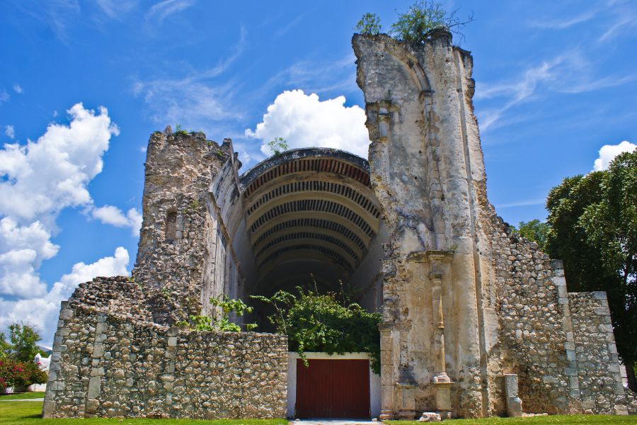 a view of crumbling stone walls of ancient ruins surrounded by greenery and blue skies with fluffy clouds