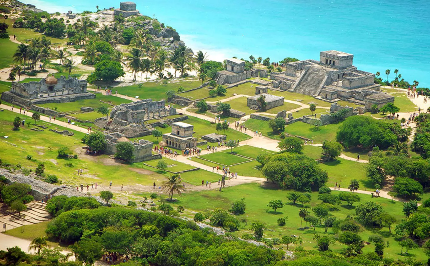 Aerial view of the Tulum ruins with lush greenery and turquoise water in the background.$# CAPTION