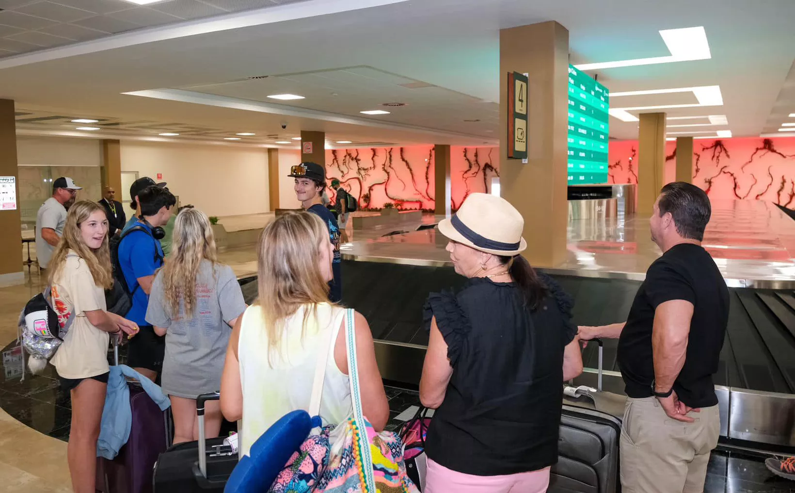 Group of travelers waiting at the baggage claim in an airport terminal.$#$ CAPTION