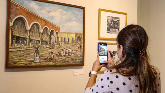 a woman taking a photo of a painting in an art gallery with another artwork visible on the wall
