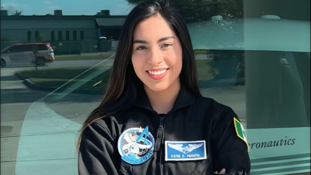 a smiling young woman wearing an astronaut suit standing in front of an aircraft-10112025