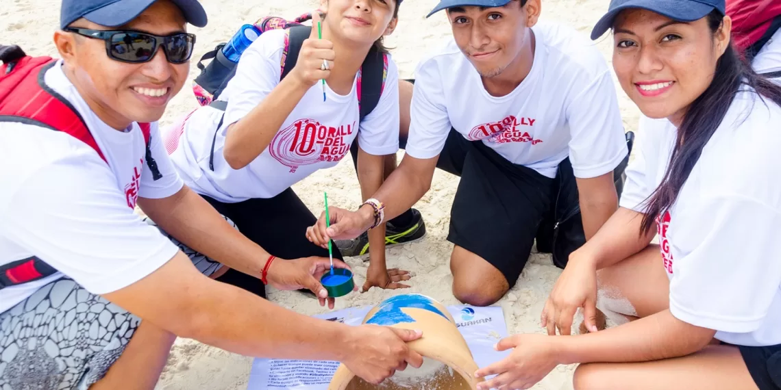 Group of individuals engaged in a beach conservation activity, smiling and painting a sand-filled container.$# CAPTION