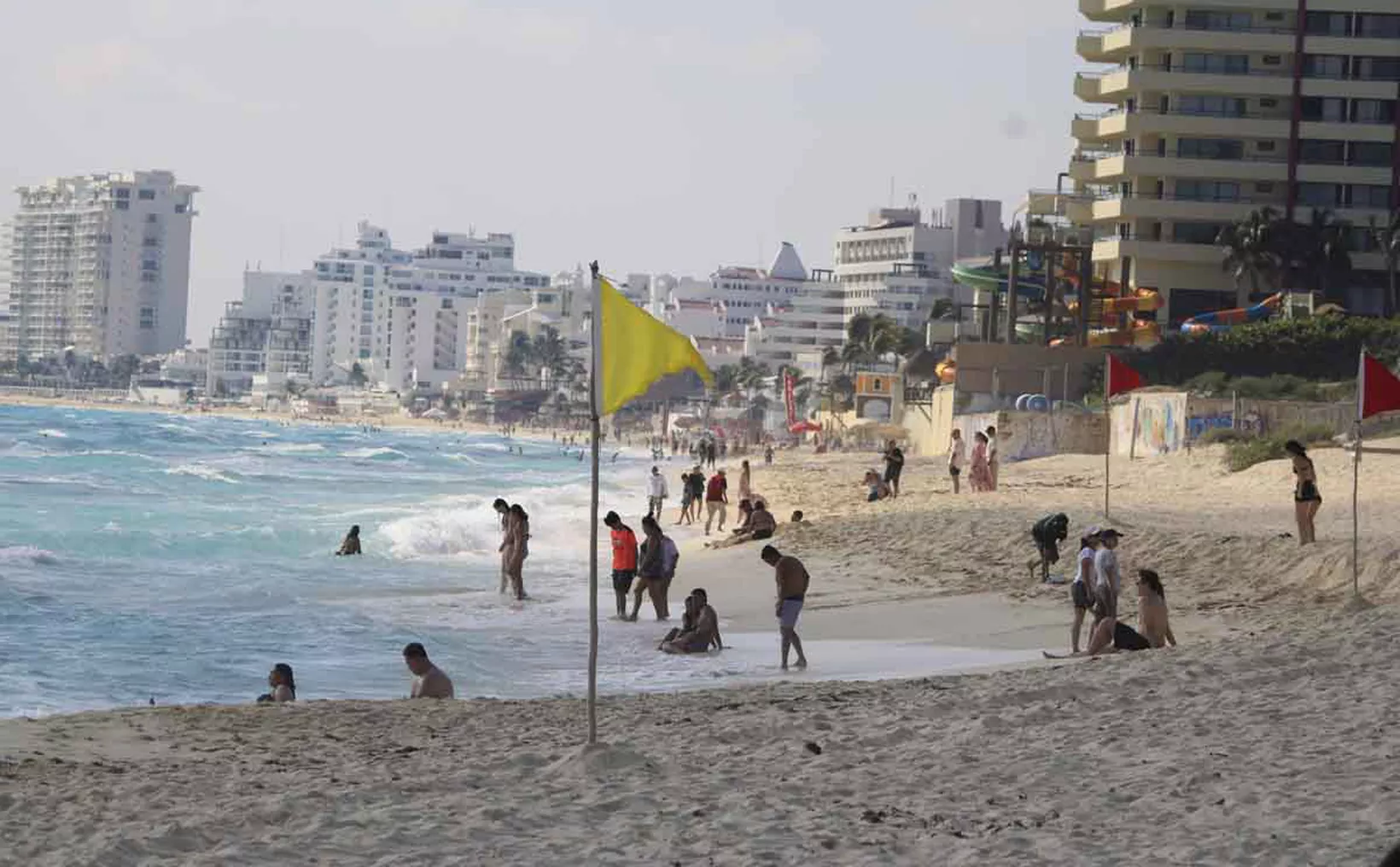 A sunny beach in Cancun, with people enjoying the water and sand, and buildings in the background.$# CAPTION
