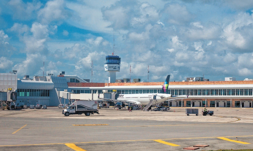 A view of Cancun International Airport featuring a plane on the tarmac and the control tower in the background under a blue sky with clouds