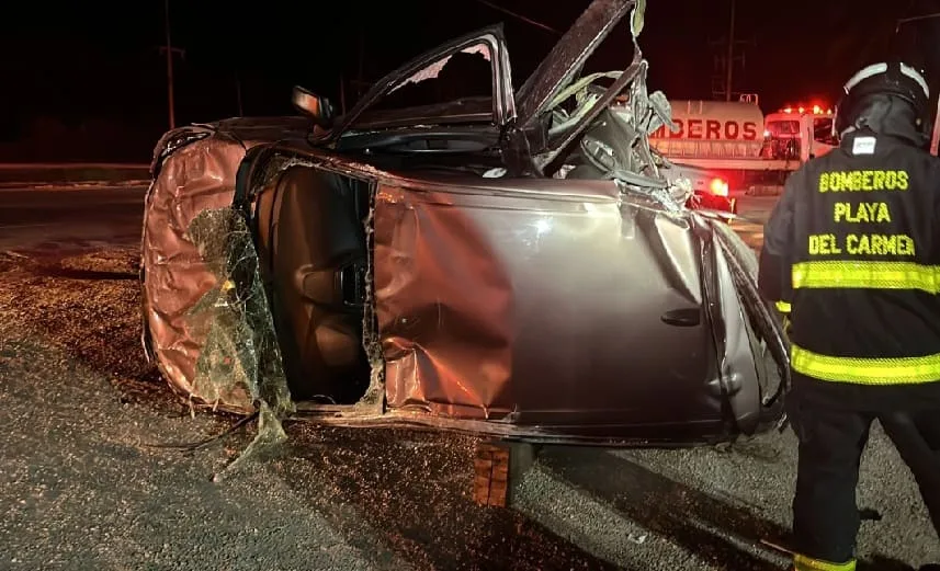 A damaged car lies on its side after an accident, with emergency responders in safety gear attending the scene at night.$#$ CAPTION