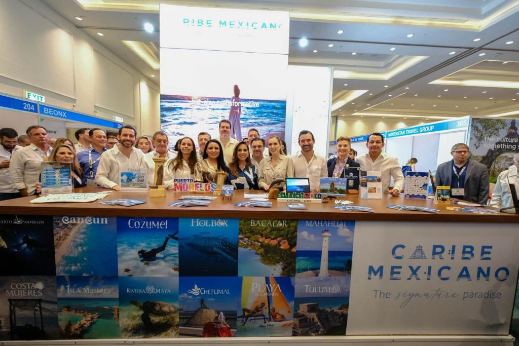 A group of professionals gathered at a booth showcasing the Caribbean region of Mexico, featuring promotional materials about various tourist destinations.