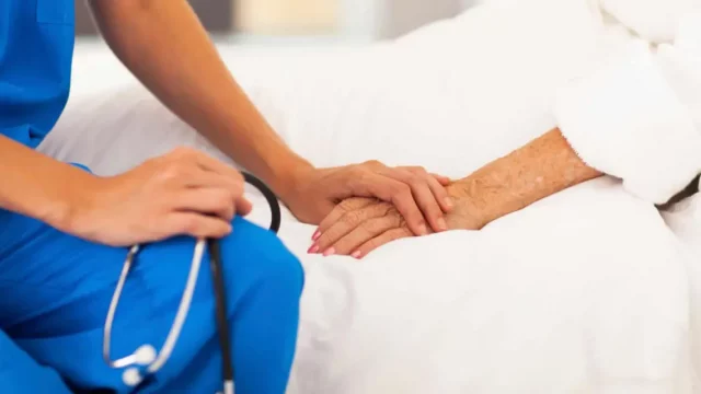 A healthcare professional holds the hand of an elderly patient, symbolizing compassion and support in a medical setting.$# CAPTION
