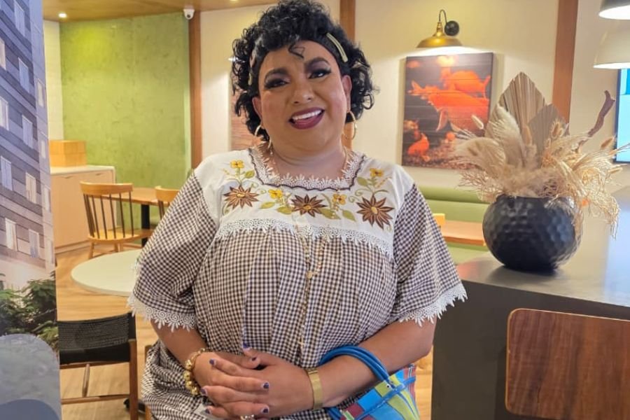 a smiling woman with curly hair wearing a traditional embroidered top in a modern interior setting
