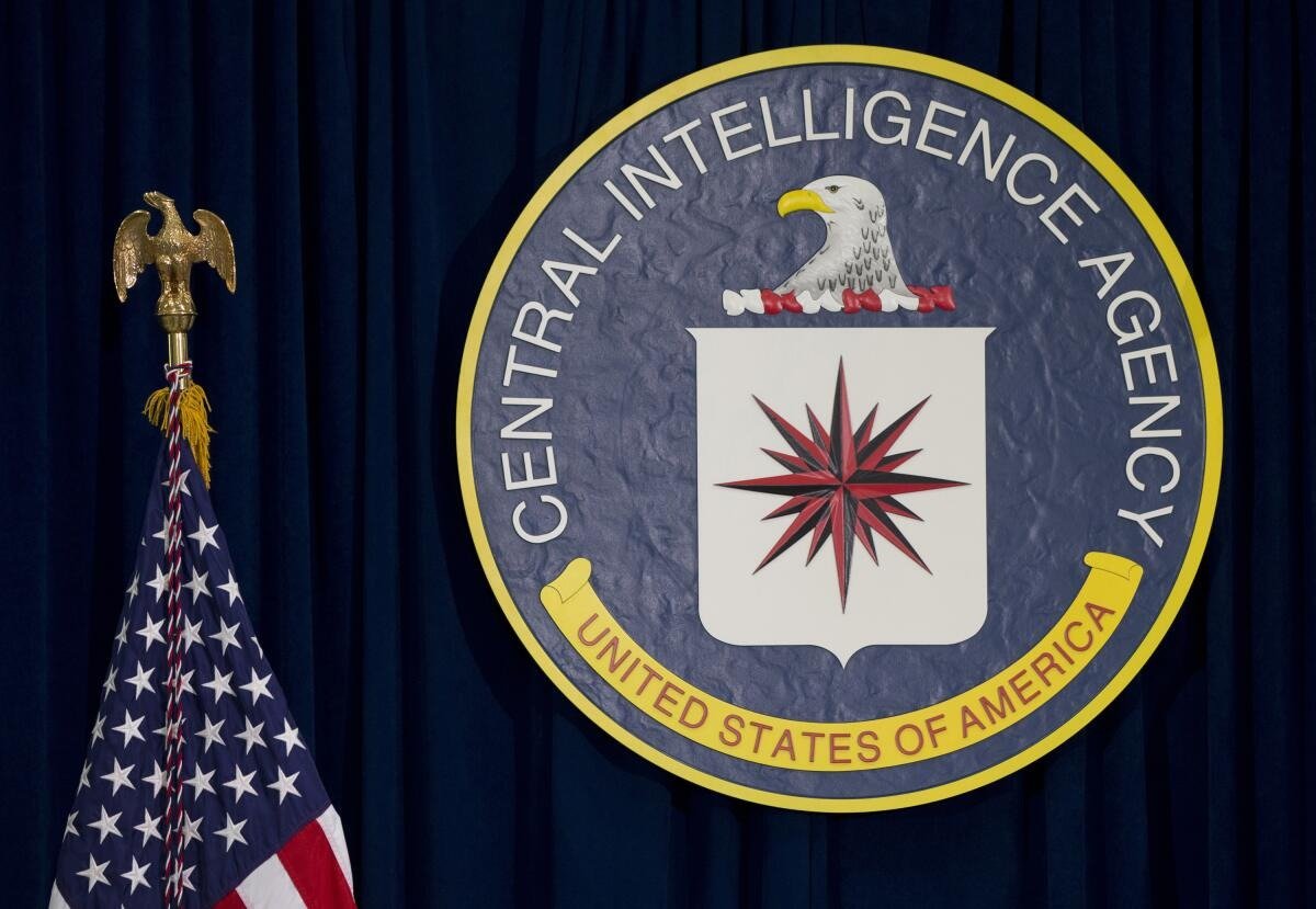 Central Intelligence Agency emblem with an eagle and the American flag beside it, set against a dark blue backdrop.$# CAPTION