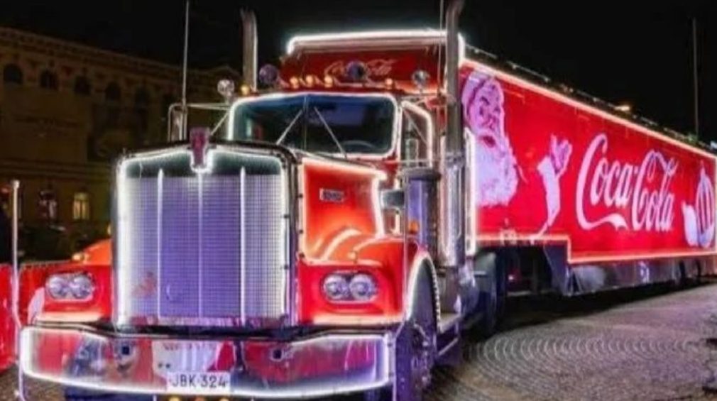 A brightly lit Coca-Cola truck decorated for the holiday season, showcasing Santa Claus and festive lights at night.$