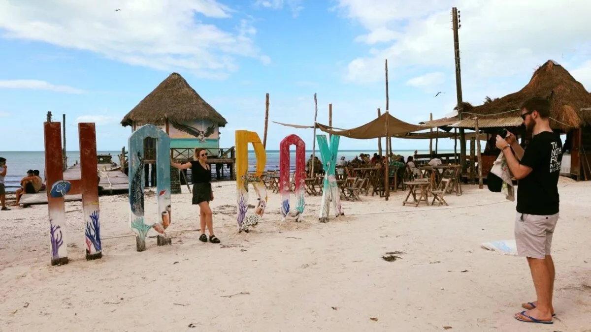 a woman posing beside a colorful beach sign spelling ROX with a man taking her picture in the background-02112025