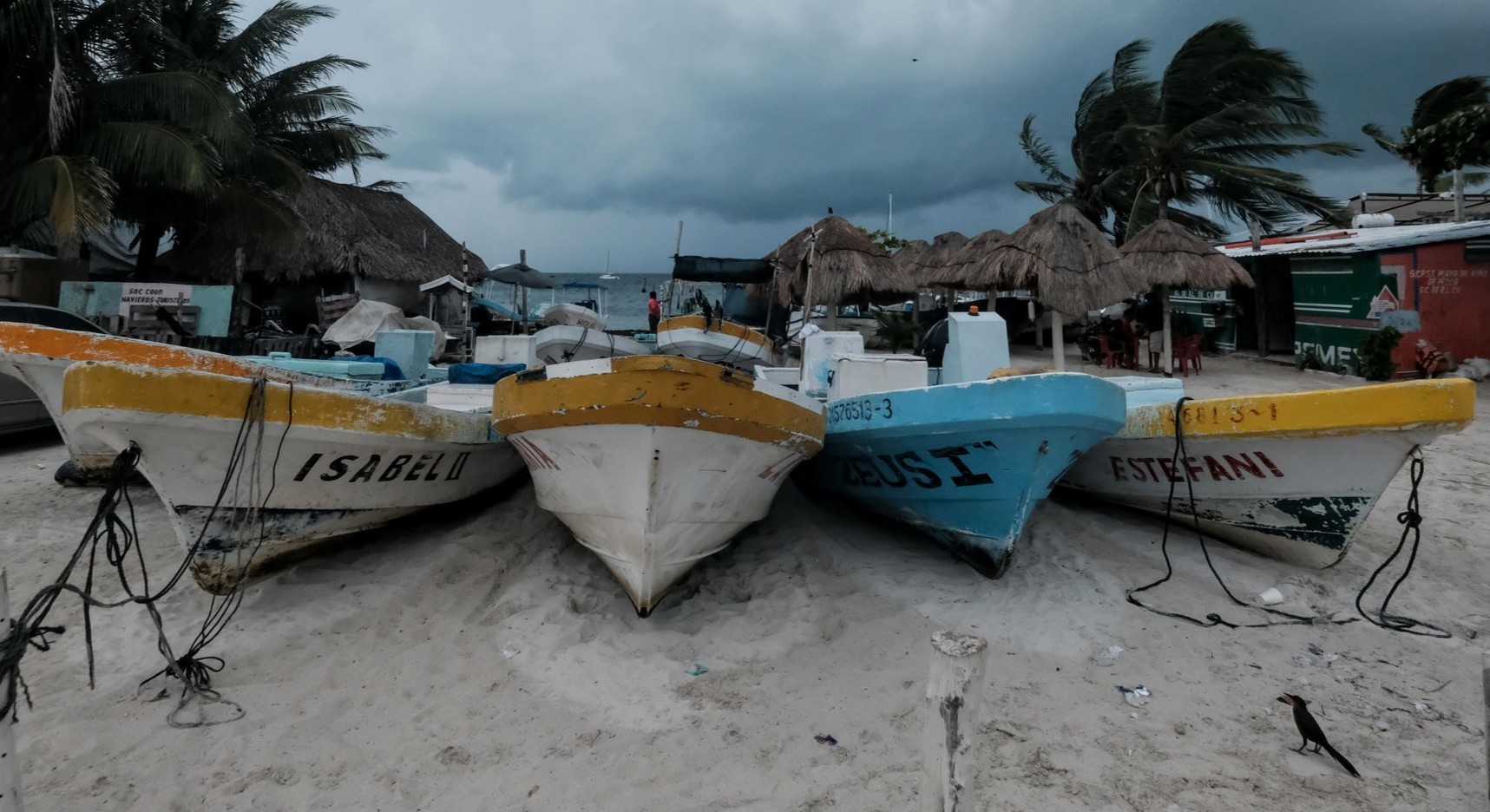 Four colorful fishing boats lined up on the beach with a cloudy sky in the background.