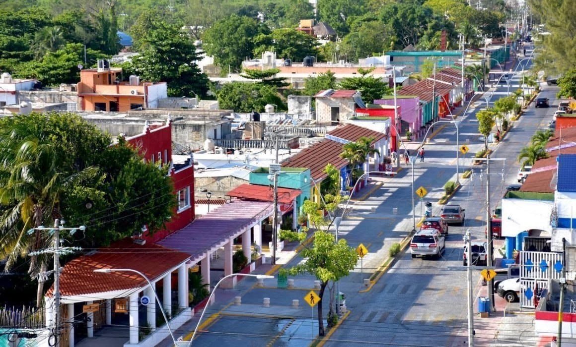 A vibrant streetscape in a coastal town featuring colorful buildings, palm trees, and a clear blue sky.$# CAPTION