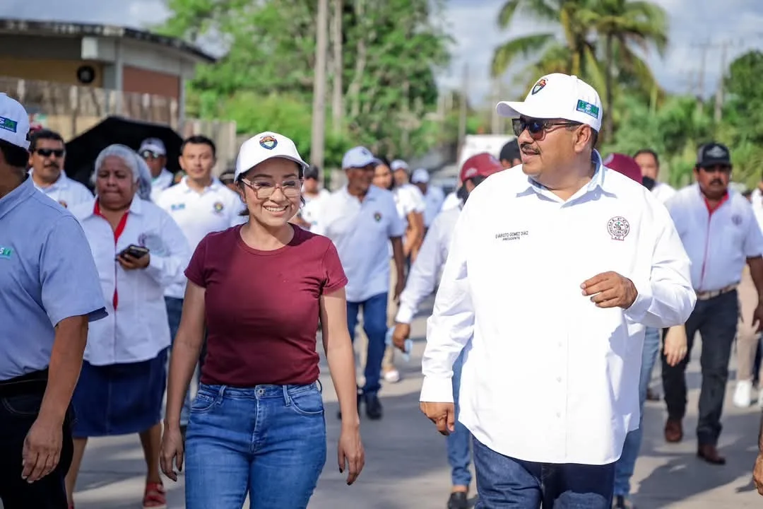 Two people walking together in a lively group during a community event, smiling and wearing branded caps.$# CAPTION