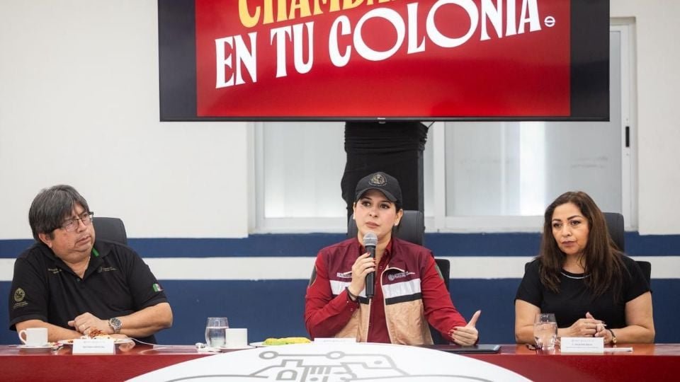 three speakers at a community engagement meeting with a red banner in the background-26112025