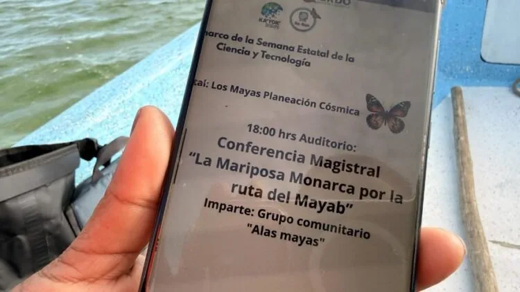 a smartphone displaying details of a conference about the monarch butterfly and its conservation on a boat near water