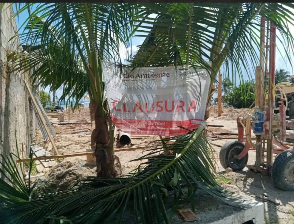 A sign reading "CLASURA" is visible among palm leaves at a construction site, indicating a closure. In the background, construction debris and equipment are present under clear blue skies.