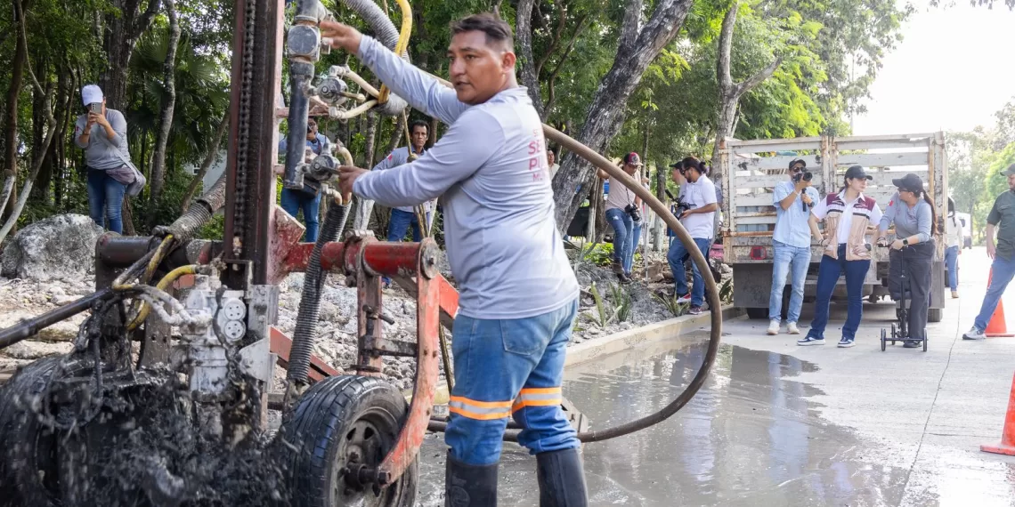 A construction worker operates machinery while others observe at a job site surrounded by trees and vehicles.$# CAPTION