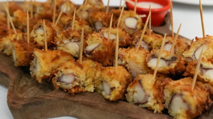 a wooden platter filled with crispy fried snacks garnished with toothpicks and a small bowl of dipping sauce in the background