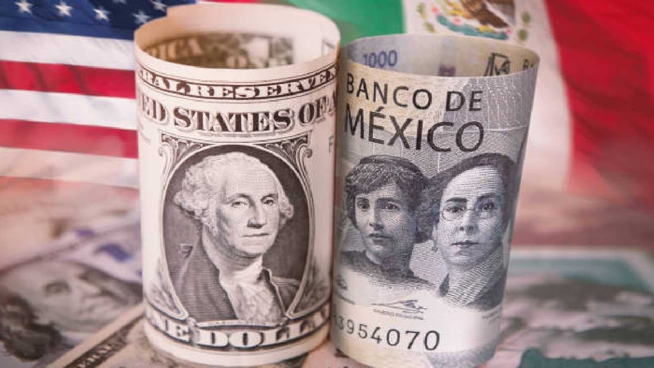 A close-up of a U.S. one-dollar bill and a Mexican one-thousand-peso note, both rolled and displayed against a backdrop of flags from the U.S. and Mexico.