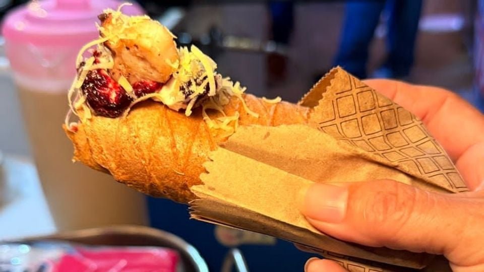 a hand holding a cone filled with food topped with shredded ingredients