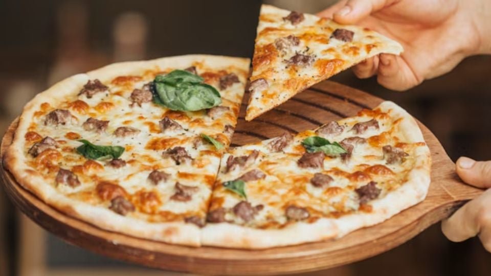 a person holding a wooden platter with a cheese and meat pizza with one slice being removed