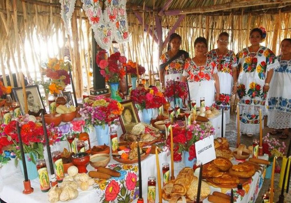 A vibrant Día de los Muertos altar adorned with flowers, food offerings, and photographs, accompanied by women in traditional clothing.$#$ CAPTION