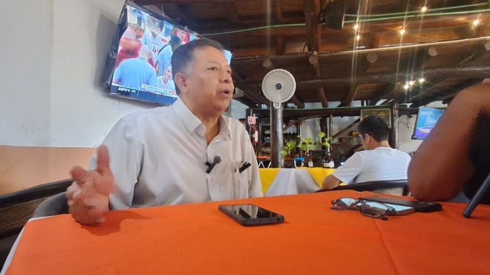 a man speaking at a table in a restaurant with a television in the background and people seated nearby