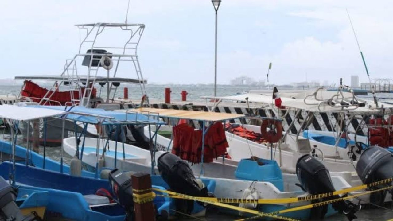 Multiple boats docked at a shoreline, with a cloudy sky overhead and safety equipment visible on the vessels.$