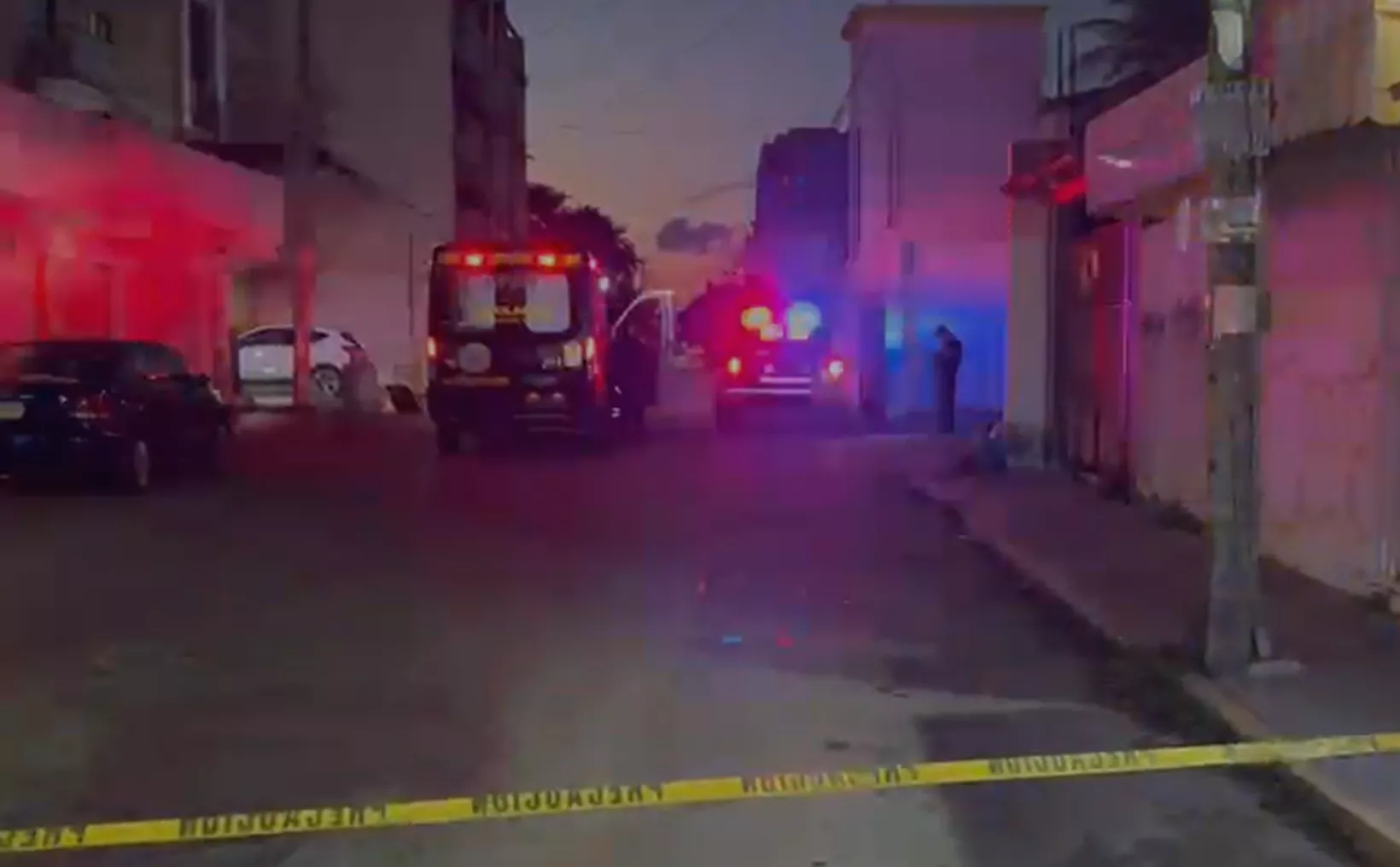 Emergency vehicles with flashing lights at a crime scene in an urban setting during twilight