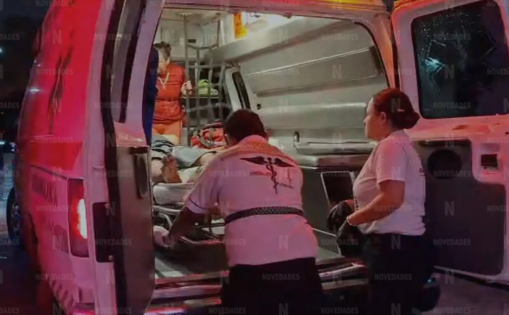 Paramedics attending to a patient inside an ambulance at night with emergency lights on