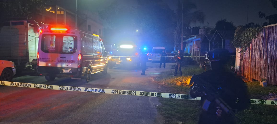 Emergency vehicles and police officers at a crime scene during nighttime. Police tape is visible on the ground, indicating a restricted area
