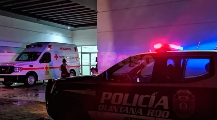 An ambulance and a police vehicle with flashing lights at a hospital entrance during nighttime. A person is seen near the ambulance.$#$ CAPTION