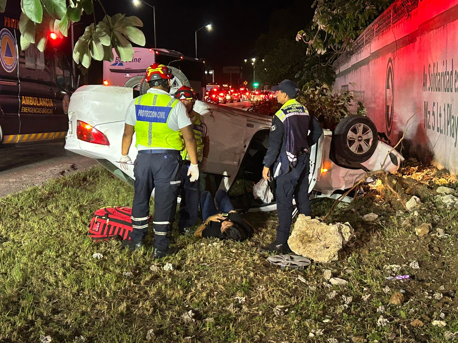 Emergency personnel assisting at a car accident scene at night, with a vehicle overturned on the roadside.$#$ CAPTION