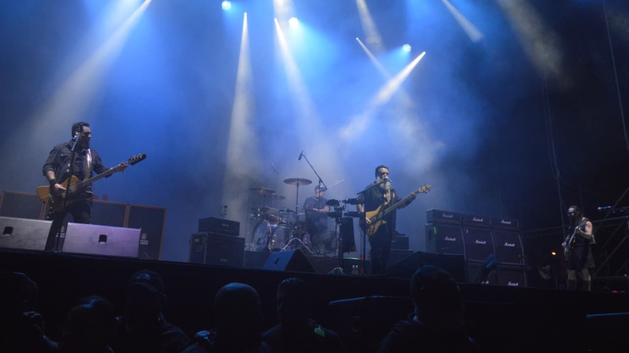 A band performing live on stage with vibrant blue lights and smoke effects in the background.$#$ CAPTION