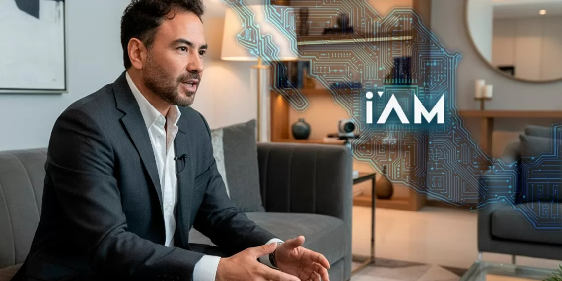 A thoughtful man in a suit seated on a couch, discussing digital technology, with graphic elements representing circuitry and the word "iAM" in the background.